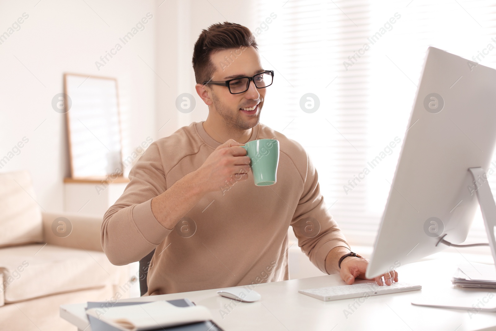 Photo of Young man with cup of drink relaxing at table in office during break