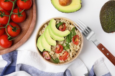 Delicious quinoa salad with tomatoes, avocado slices and spinach leaves served on white table, flat lay