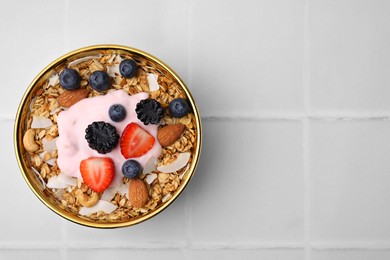 Tasty granola, yogurt and fresh berries in bowl on white tiled table, top view with space for text. Healthy breakfast