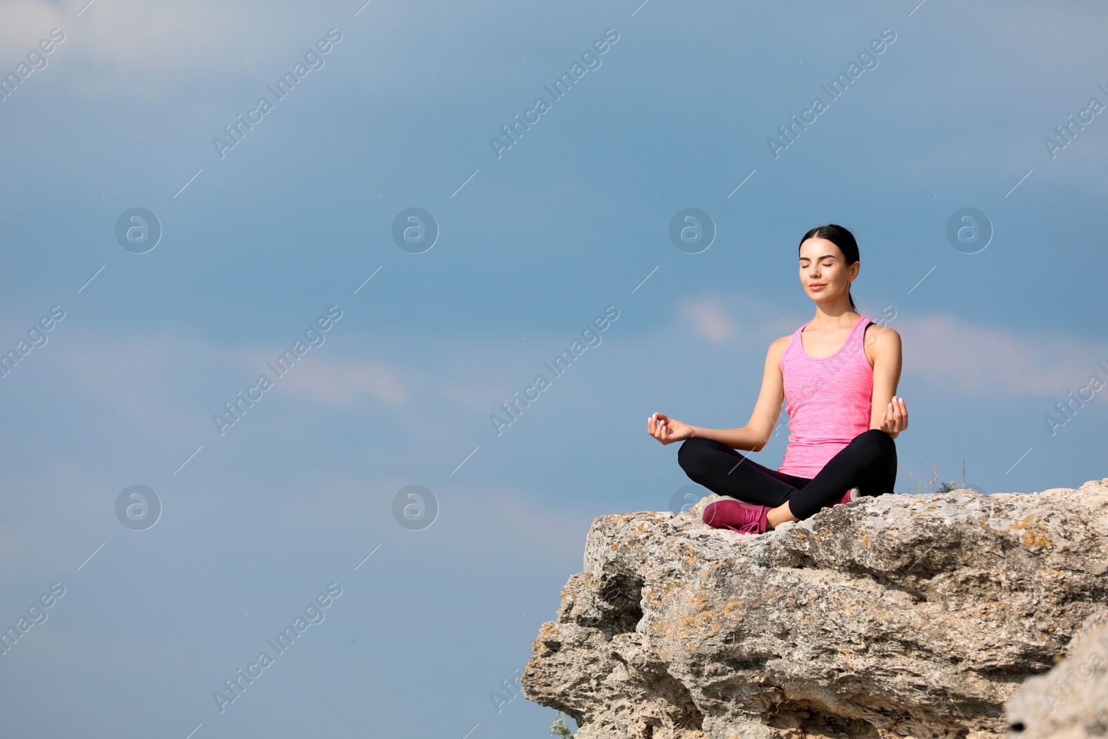 Photo of Young woman meditating on cliff. Space for text