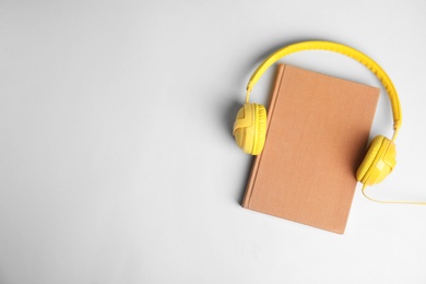 Photo of Modern headphones with hardcover book on light background, top view. Space for text