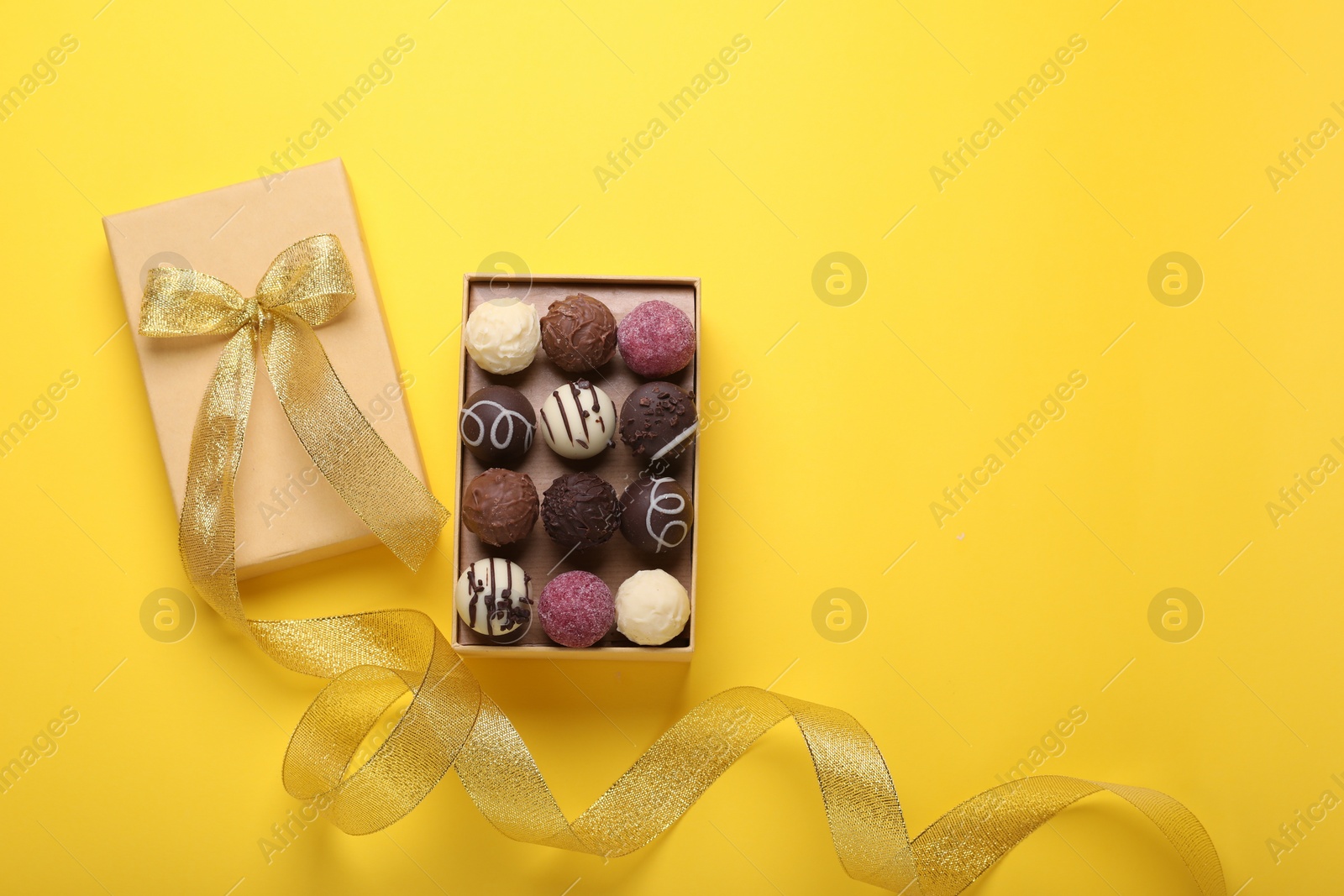 Photo of Open box with delicious chocolate candies on yellow background, top view. Space for text