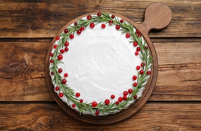 Photo of Traditional Christmas cake decorated with rosemary and cranberries on wooden table, top view