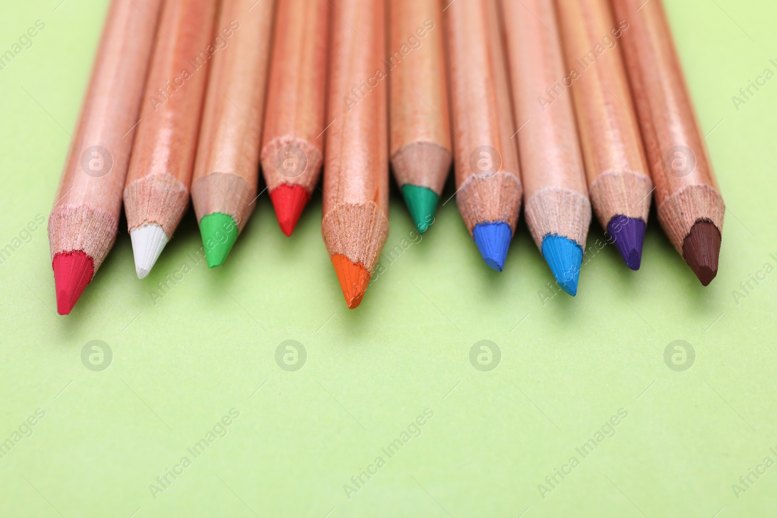 Photo of Many colorful pastel pencils on light green background, closeup and space for text. Drawing supplies