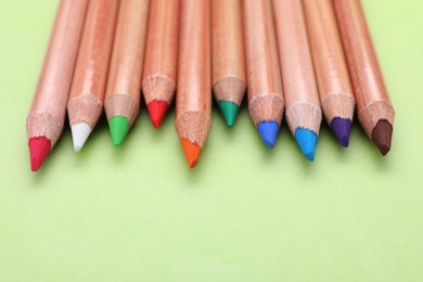 Many colorful pastel pencils on light green background, closeup and space for text. Drawing supplies