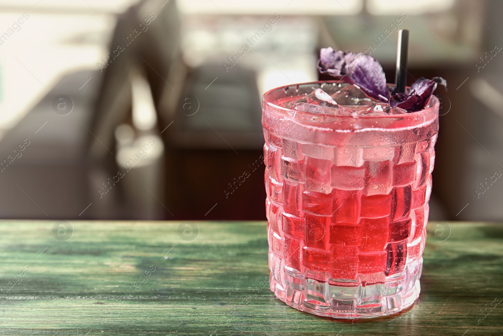 Photo of Glass with delicious cocktail and ice cubes on counter in bar