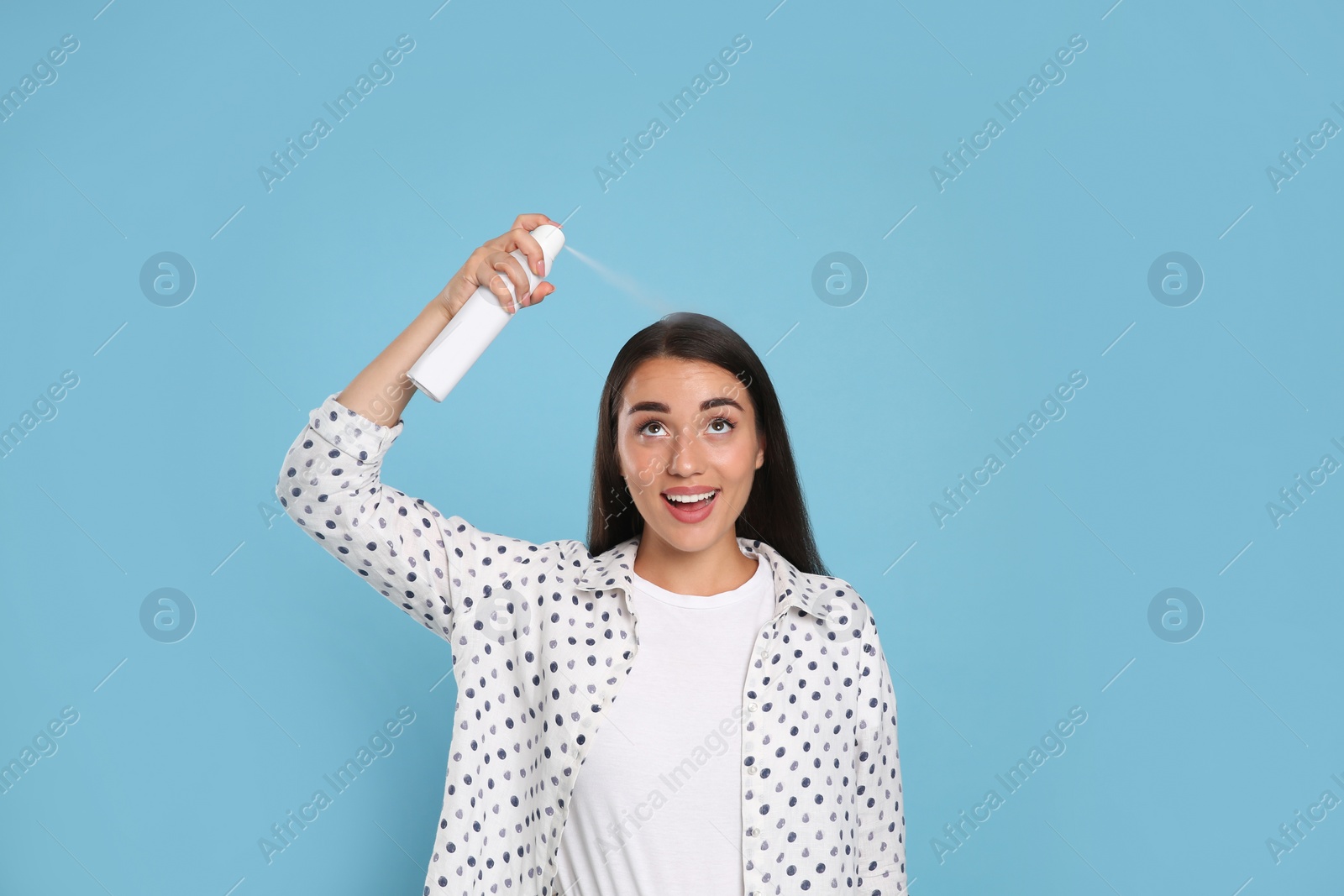 Photo of Young woman applying dry shampoo against light blue background