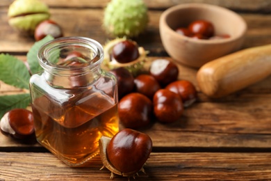 Photo of Chestnuts and jar of essential oil on wooden table. Space for text