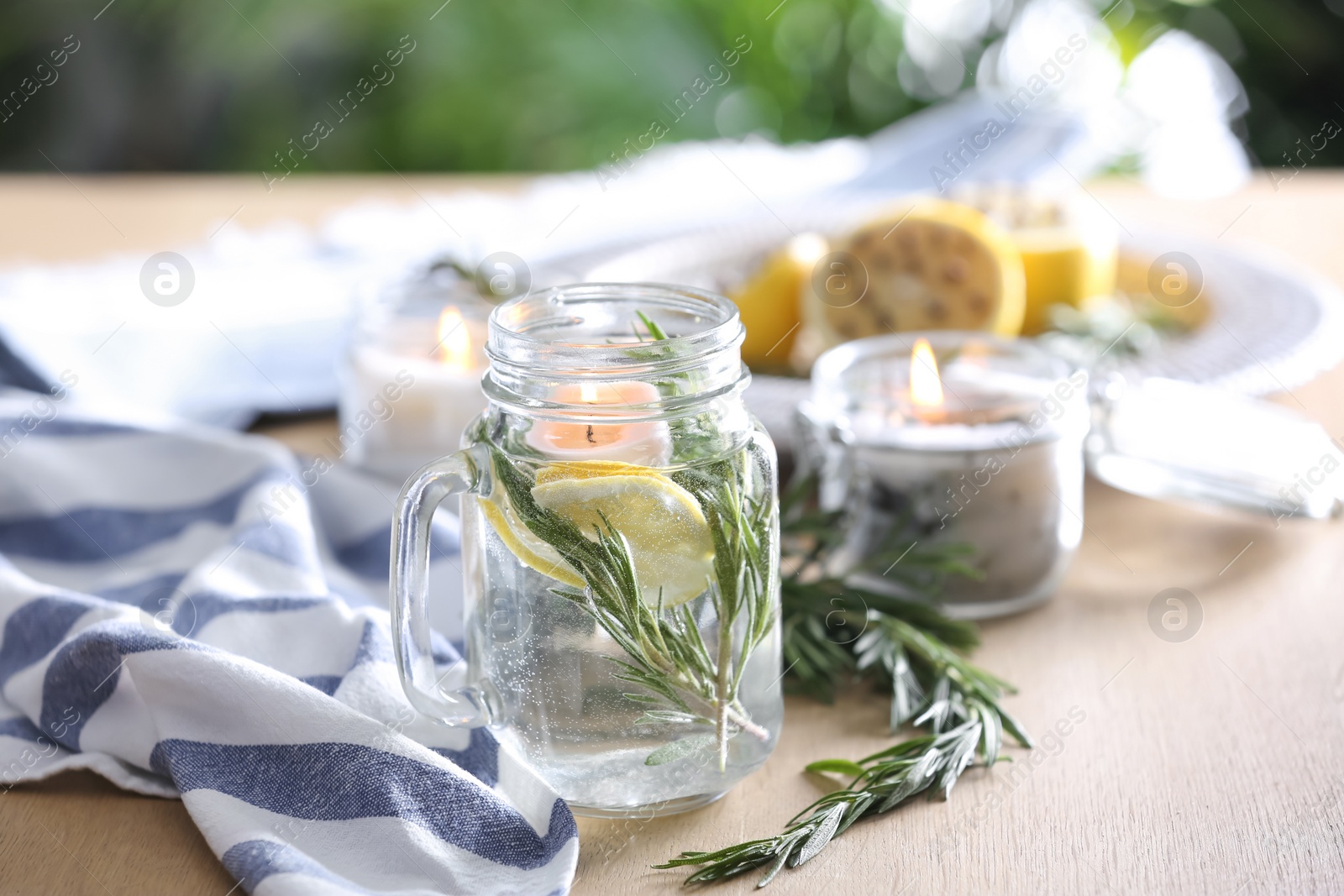 Photo of Mason jar with slice of lemon, fresh rosemary and water on wooden table outdoors. Natural homemade repellent