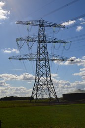 High voltage tower with electricity transmission power lines in field on sunny day