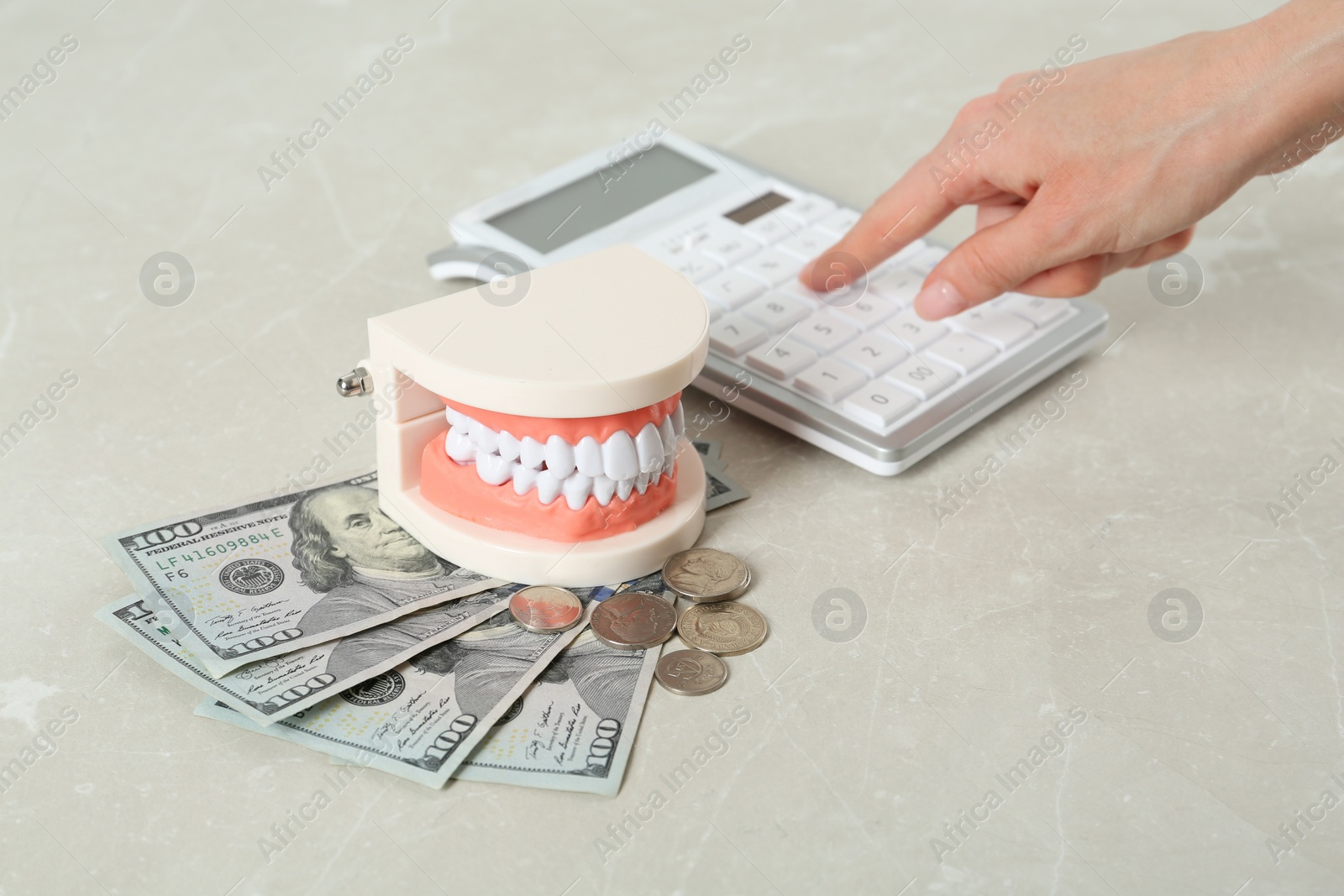 Photo of Woman using calculator near educational dental typodont model and money at light grey table, closeup. Expensive treatment