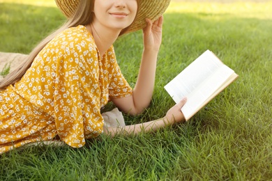 Young woman reading book on green grass, closeup