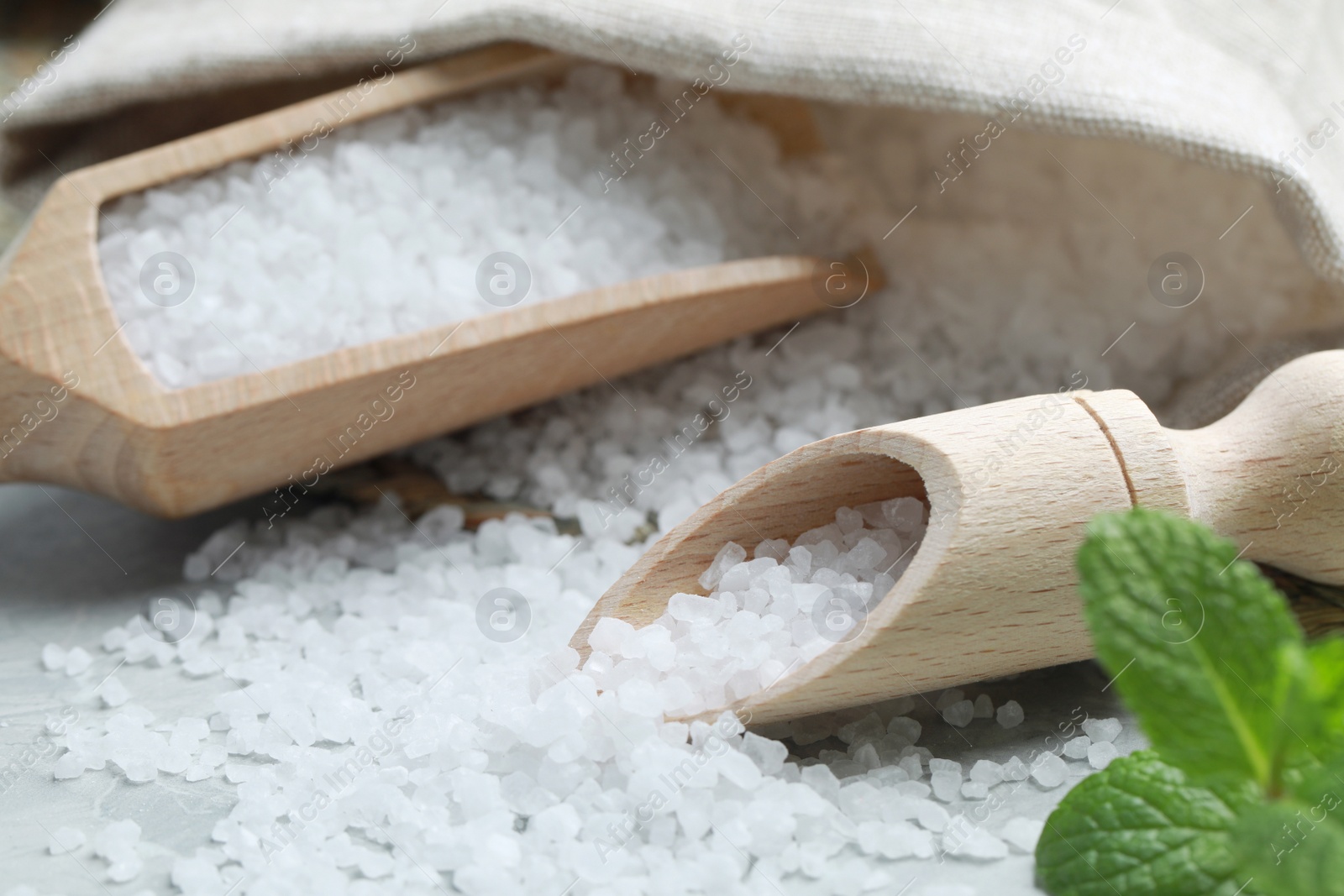 Photo of Wooden scoops with natural sea salt and sack on light grey marble table, closeup