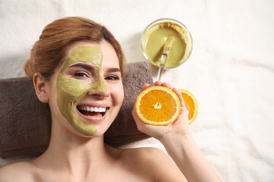 Woman with mask on face and cut orange relaxing in spa salon, top view. Space for text