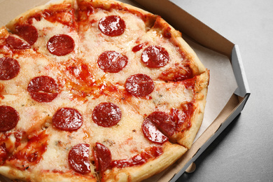 Hot delicious pepperoni pizza in cardboard box on grey table, closeup
