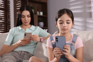 Photo of Internet addiction. Mother and her daughter with smartphones on sofa in living room