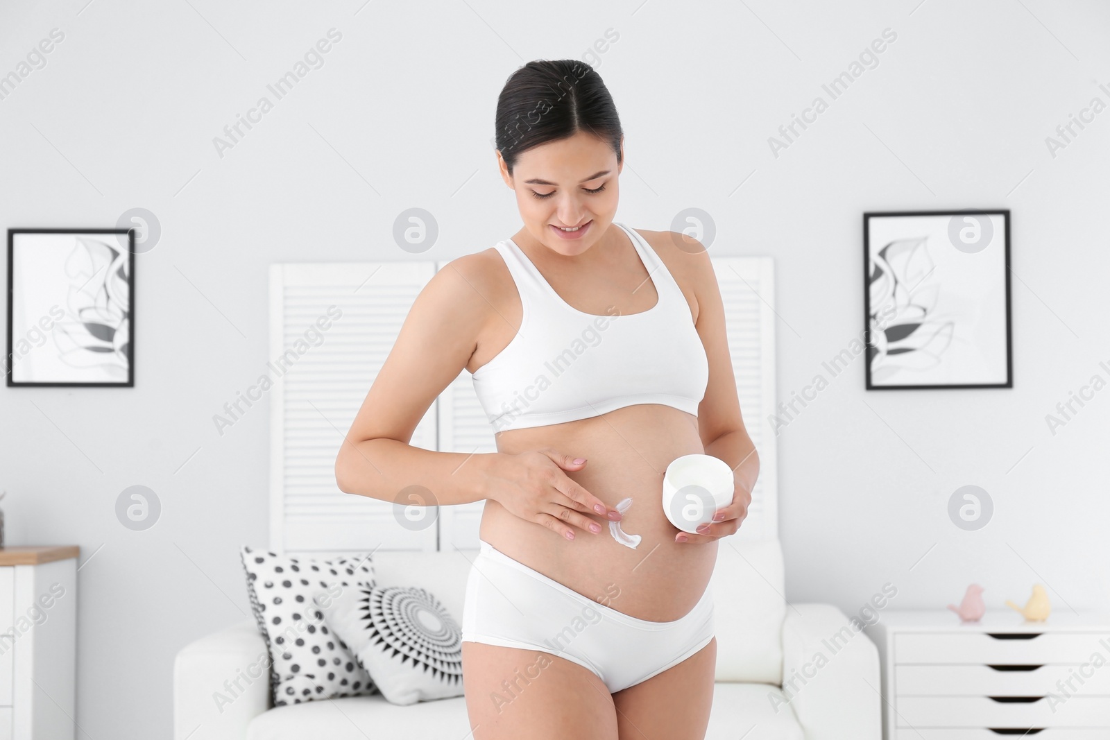 Photo of Pregnant woman applying body cream on belly at home