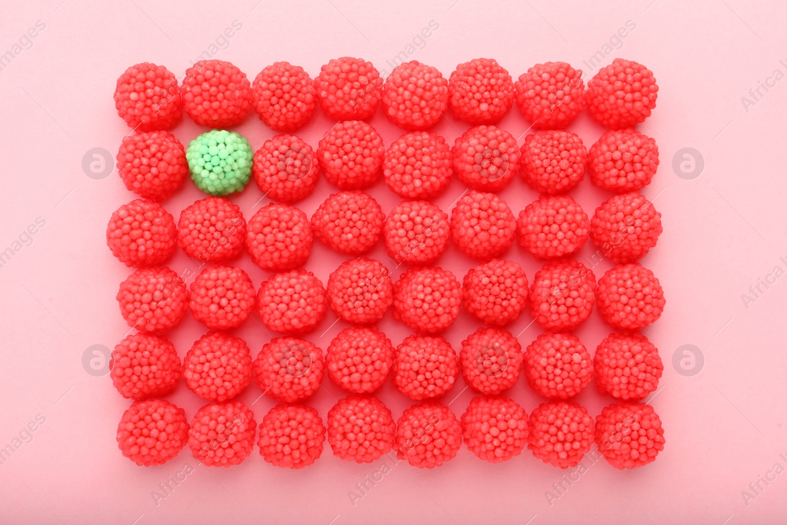 Photo of Delicious green gummy raspberry candy among red ones on pink background, flat lay