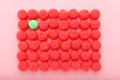 Photo of Delicious green gummy raspberry candy among red ones on pink background, flat lay