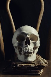 Photo of Human skull and old books on wooden chair against black background