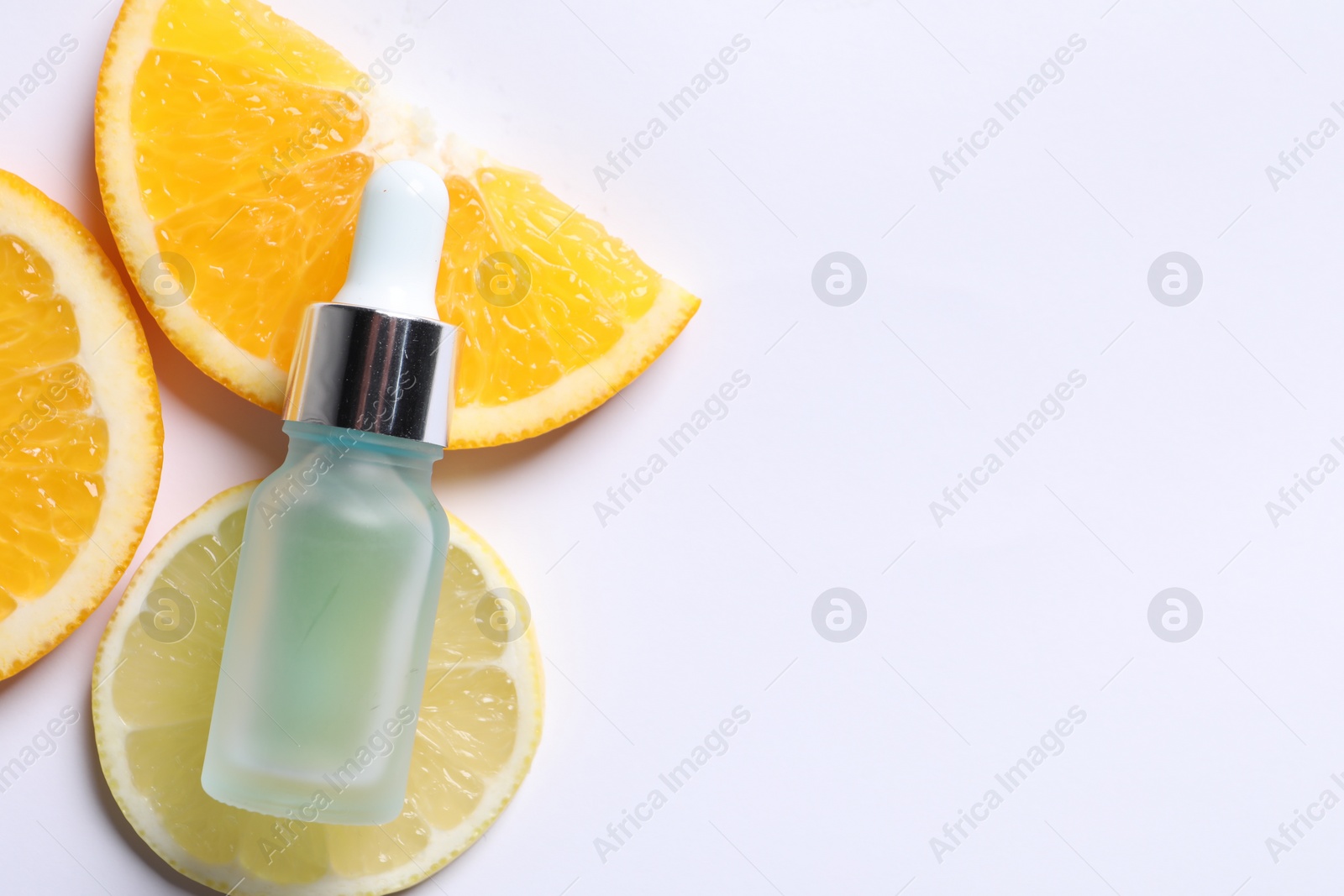 Photo of Bottle of cosmetic serum and sliced citrus fruits on white background, flat lay. Space for text