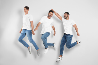 Group of young men in stylish jeans jumping near light wall