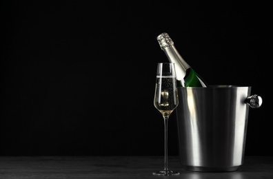 Photo of Glass of champagne near bucket with bottle on black background, space for text