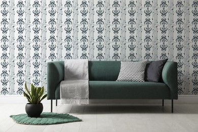 Comfortable teal sofa and plant near wall. Minimalist living room interior