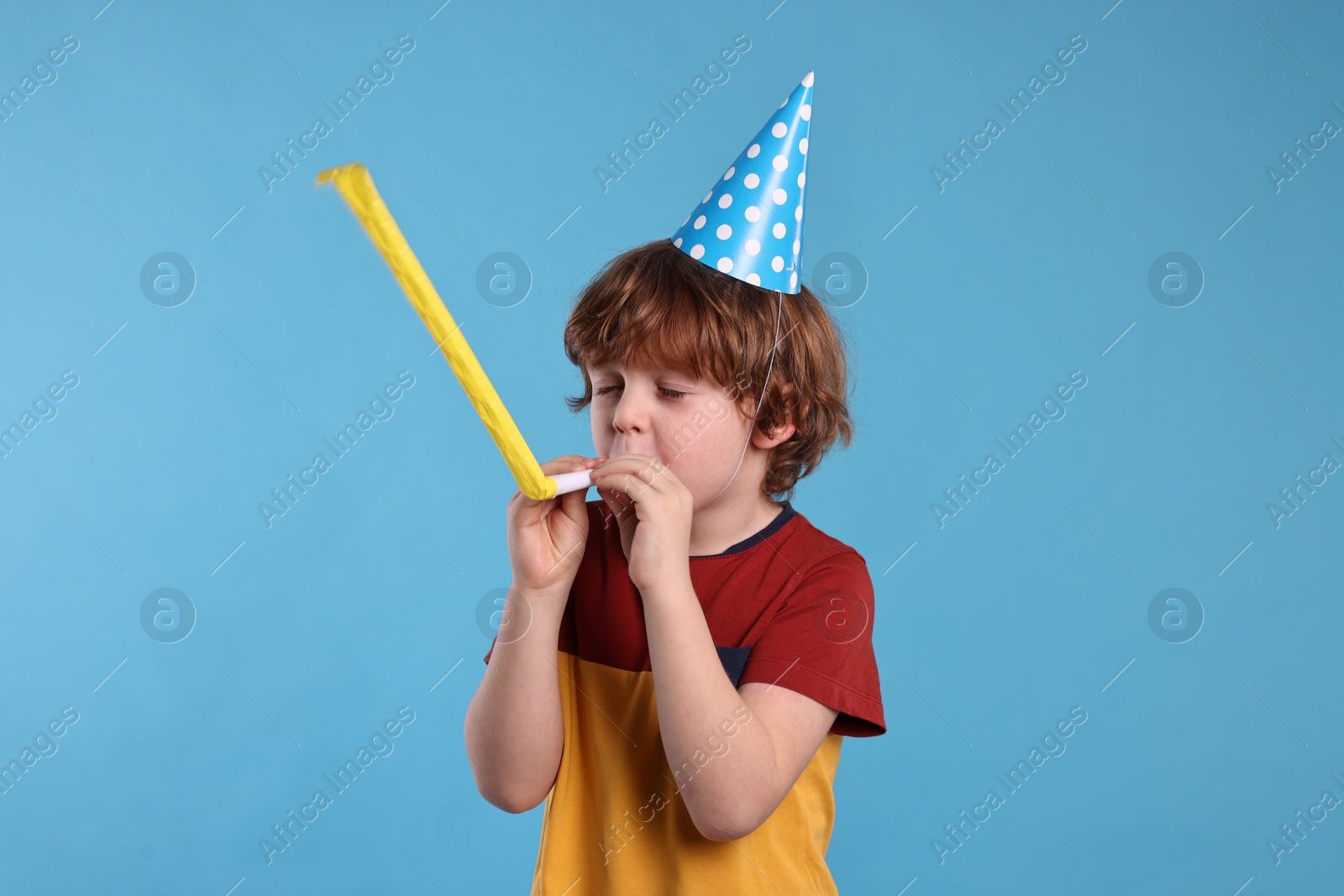 Photo of Birthday celebration. Cute little boy in party hat with blower on light blue background