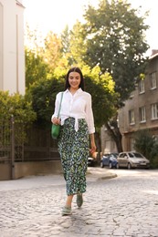 Beautiful young woman in stylish outfit walking on city street