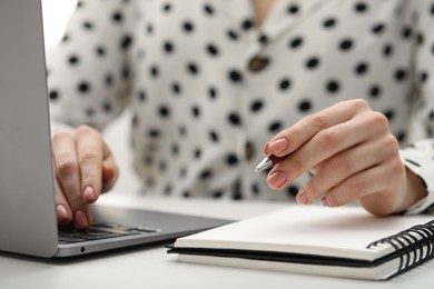 E-learning. Woman taking notes during online lesson at table indoors, closeup