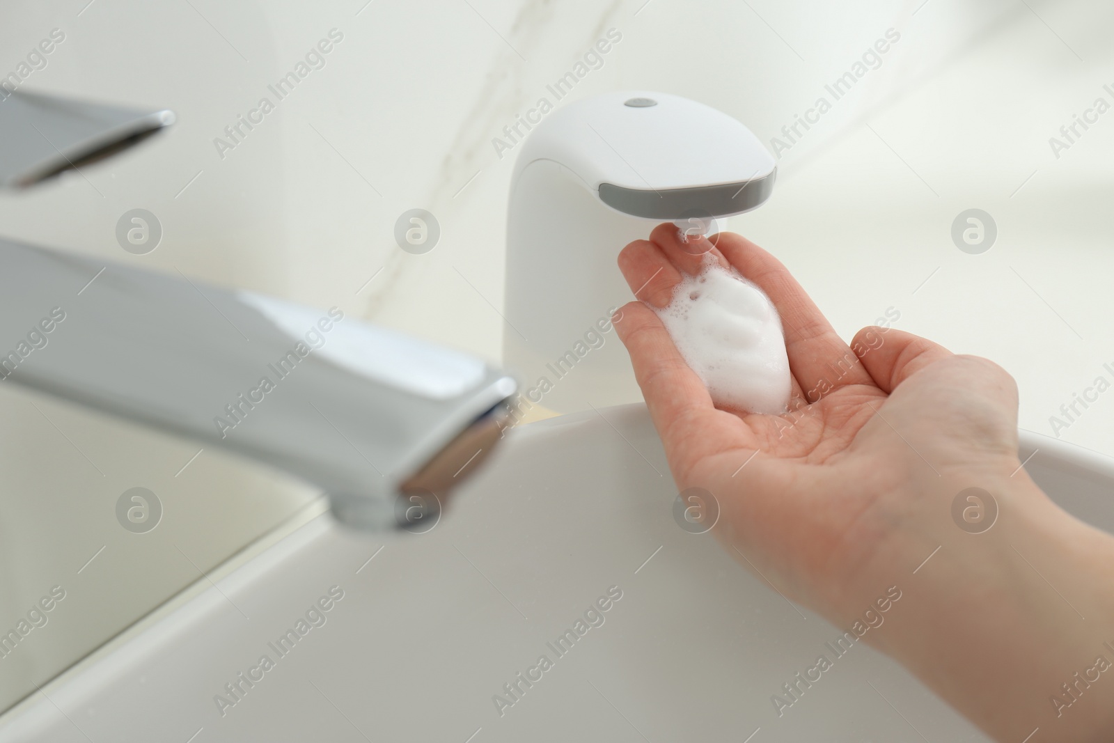Photo of Woman using automatic soap dispenser in bathroom, closeup