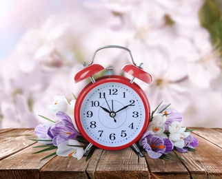 Alarm clock and spring flowers on wooden table. Time change 