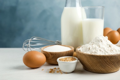 Photo of Fresh ingredients for delicious homemade cake on white wooden table against blue background