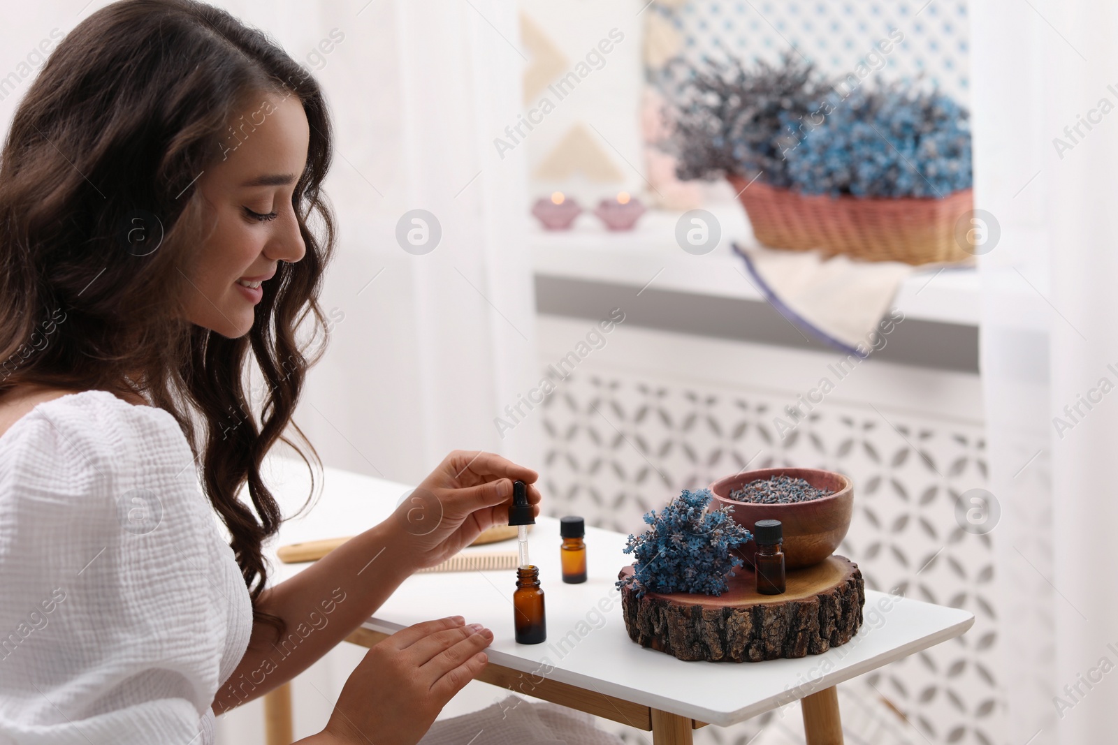 Photo of Beautiful young woman with bottle of essential oil at table indoors