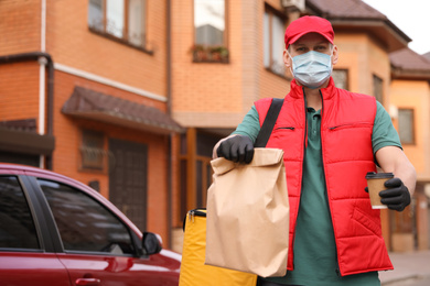 Courier in protective mask and gloves with orders near car outdoors. Food delivery service during coronavirus quarantine