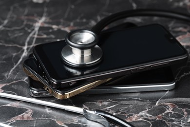 Photo of Stack of modern smartphones and stethoscope on black table