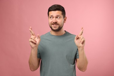 Emotional man crossing his fingers on pink background