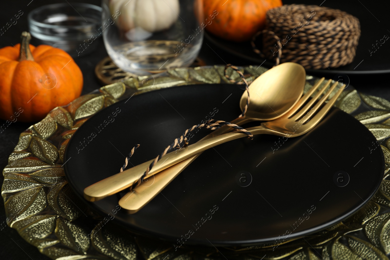 Photo of Autumn table setting with golden cutlery and pumpkin on black background, closeup