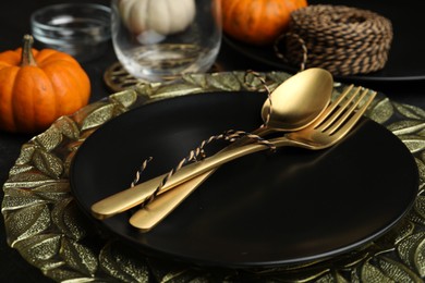 Autumn table setting with golden cutlery and pumpkin on black background, closeup