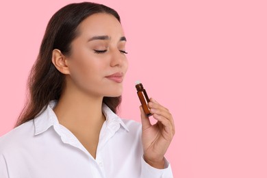 Photo of Beautiful young woman with bottle of essential oil on pink background, space for text