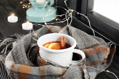Photo of Composition with cup of hot winter drink, scarf and Christmas lights near window. Cozy season