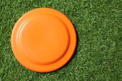 Photo of Orange plastic frisbee disk on green grass, top view. Space for text