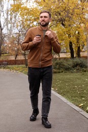Photo of Handsome man wearing stylish clothes with cup of coffee in autumn park