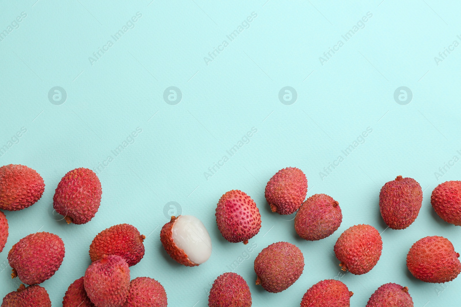 Photo of Fresh ripe lychees on turquoise background, flat lay. Space for text