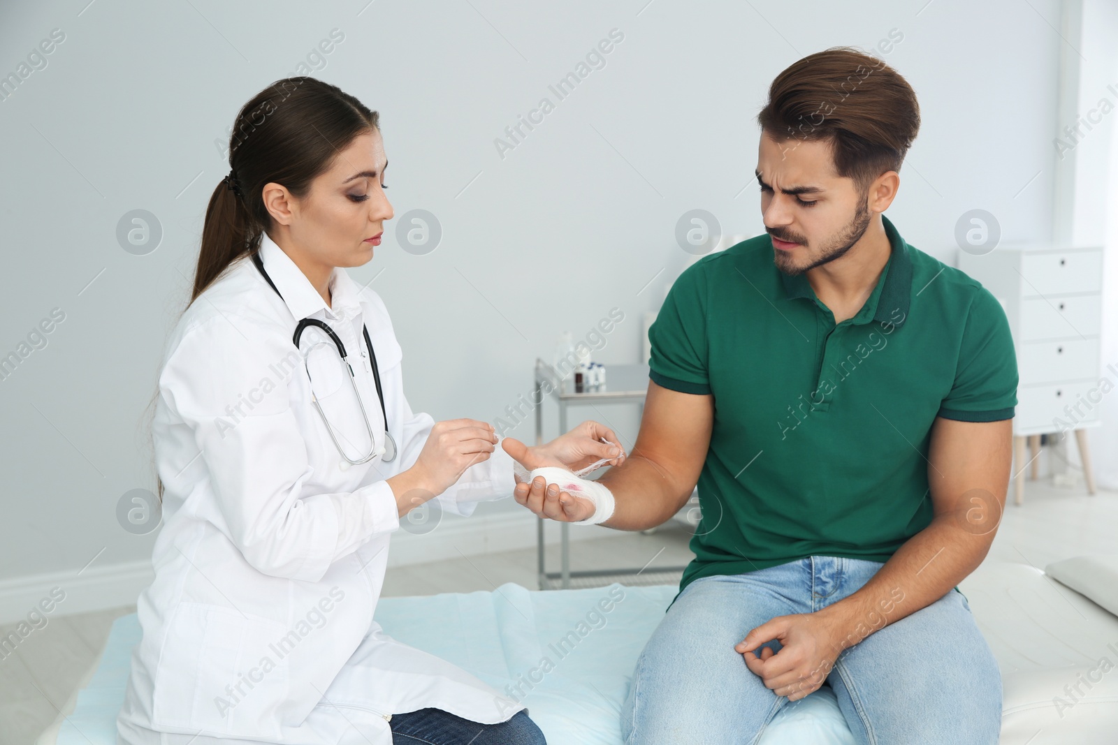 Photo of Female doctor applying bandage on young man's hand in clinic. First aid