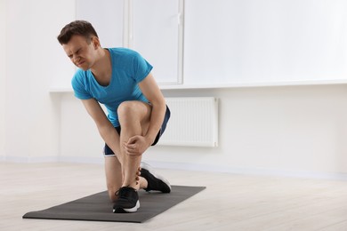 Photo of Man suffering from leg pain on mat indoors. Space for text