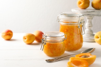 Jars of apricot jam and fresh fruits on white wooden table