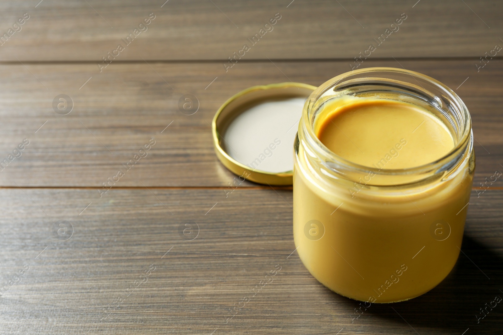 Photo of Spicy mustard in glass jar on wooden table. Space for text