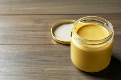 Spicy mustard in glass jar on wooden table. Space for text